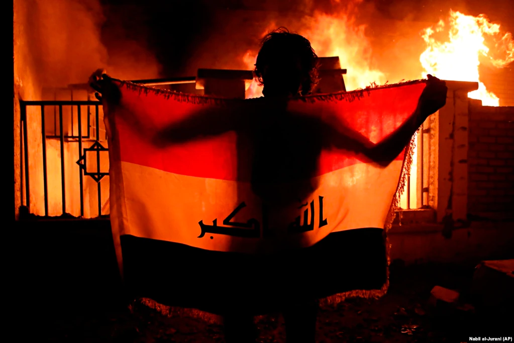 A man holds an Iraqi national flag while protesters burn a municipal complex during protests demanding better public services and jobs in the city of Basra, 550 kilometers southeast of Baghdad. (AP/Nabil al-Jurani)